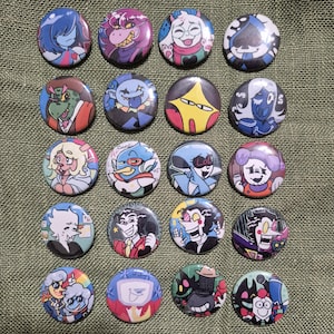 Può includere: Una collezione di sedici bottoni rotondi e colorati con vari disegni di personaggi dei cartoni animati. I bottoni presentano una varietà di personaggi con diverse espressioni e combinazioni di colori, su uno sfondo verde.