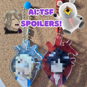 May include: Acrylic heart-shaped keychains with anime-style character art. One keychain is red, the other is clear. A white bear-shaped charm and a character image are also present. The text "AI:TSF SPOILERS!" is visible.