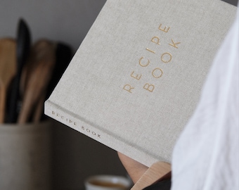 May include: A light gray recipe book with gold lettering that reads "RECIPE BOOK" on the cover. The book has gold corner protectors. The spine of the book also has the words "RECIPE BOOK".
