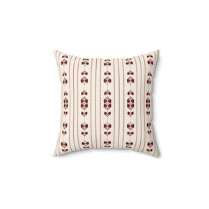 May include: A square throw pillow featuring a cream-colored background with a repeating vertical pattern. The design consists of thin brown stripes alternating with rows of geometric arrow-like shapes in shades of dark red and muted pink.