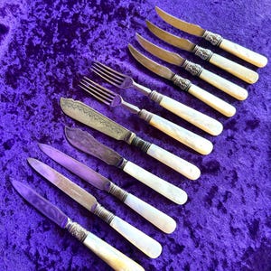 May include: A set of eight silver knives and two forks with mother-of-pearl handles. The knives have ornate silver handles and the forks have simple silver handles.