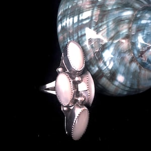 May include: A silver ring with three white mother-of-pearl stones set in a cluster design.