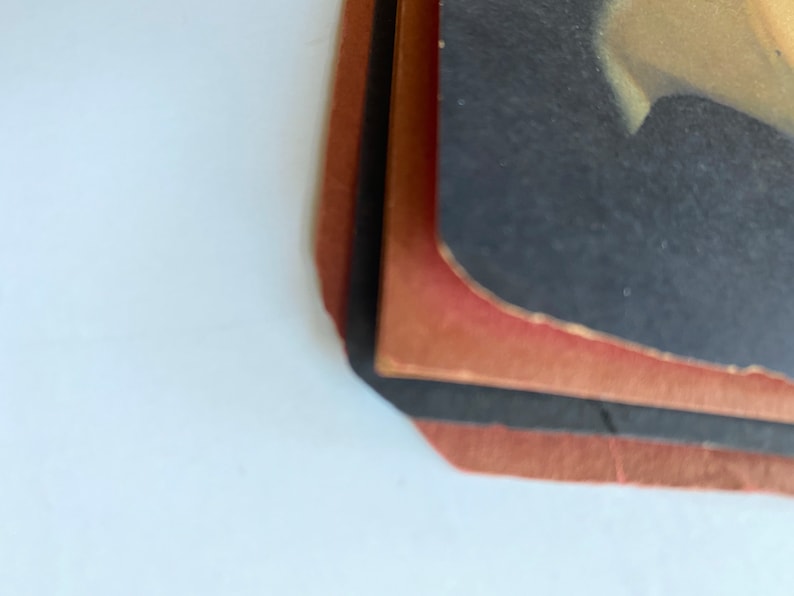 May include: A stack of vintage photographs with a black and red border. The edges of the photos are slightly worn, and the colors are faded. The top photo has a dark background with a light-colored area.