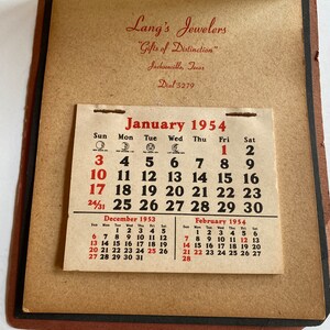 May include: Vintage pocket calendar from Lang's Jewelers, Jacksonville, Texas, featuring the January 1954 calendar page. The calendar also shows December 1953 and February 1954. The calendar is in a brown leather-like cover.
