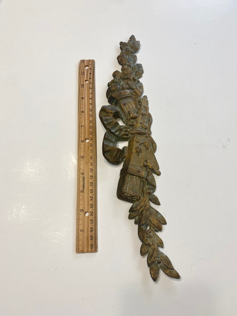 K&ouml;nnte beinhalten: Ein verziertes St&uuml;ck aus vergoldetem Metall mit einem floralen Design und einem Band. Das St&uuml;ck ist etwa 18 cm lang.