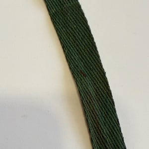 May include: Close-up of a dark green woven strap. The strap has a diagonal pattern and appears to be made of a textured material. A few small, dark red marks are visible on the strap.