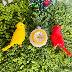 May include: Three vintage Christmas ornaments: a yellow bird, a red bird, and a white ornament with a yellow and silver design.