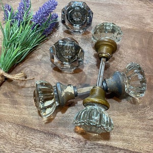 May include: Five antique glass door knobs with brass hardware. The knobs are clear glass with a faceted design. The hardware is a mix of brass and aged metal.