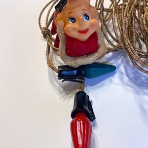 May include: A string of Christmas lights with red and green bulbs and a Santa Claus face on each bulb.