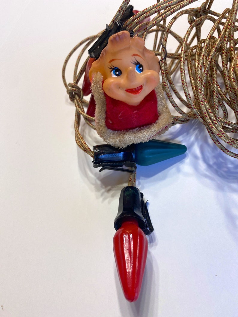 May include: A string of Christmas lights with red and green bulbs and a Santa Claus face on each bulb.