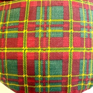 May include: Close-up of a plaid fabric with a pattern of red, green, and yellow lines. The fabric is a mix of red and green squares with yellow lines. A green fabric trim with two buttons is at the top.