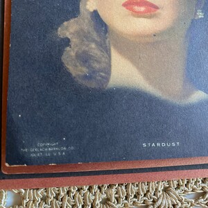 May include: Vintage print of a woman with red lipstick and blue eyes. The print is titled "Stardust" and includes the copyright information for The Gerlach-Barklow Co., Juliet, IL, USA.
