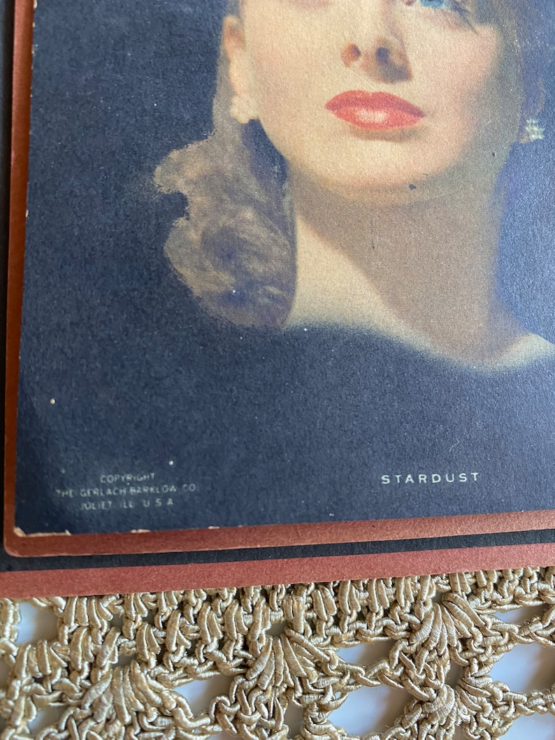 May include: Vintage print of a woman with red lipstick and blue eyes. The print is titled "Stardust" and includes the copyright information for The Gerlach-Barklow Co., Juliet, IL, USA.