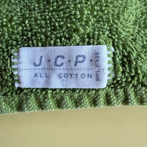 May include: Close-up of a green terry cloth towel with a white label. The label reads "J.C.P. ALL COTTON" in dark blue letters. The towel has a textured surface and a light green color.