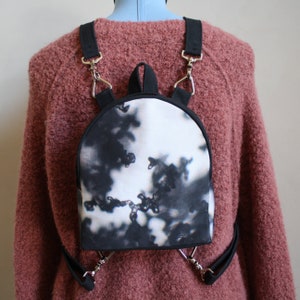 May include: A small black and white tie-dye backpack with adjustable straps and silver hardware.