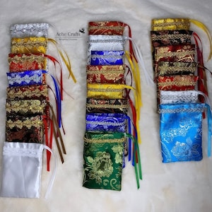 May include: An assortment of small, decorative fabric pouches in various colors, including gold, red, blue, and green. Each pouch features a drawstring closure and is adorned with ornate patterns and trim. Some pouches have ribbons attached.