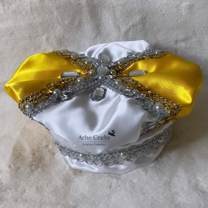 May include: White satin crown with a yellow satin bow, silver trim, and pearl and rhinestone embellishments. The crown has the text "Ache Crafts Religious Creations" on the front.