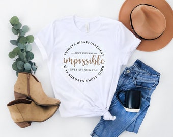 Può includere: T-shirt bianca con grafica rotonda leopardata con la scritta "impossible". La maglietta è abbinata a jeans blu, un cappello marrone e stivaletti color cammello. È presente anche una tazza bianca e nera.