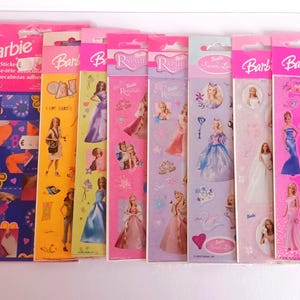 Puede incluir: Una colección de hojas de pegatinas de Barbie en varios diseños y colores. Las hojas presentan muñecas Barbie con diferentes atuendos y poses, algunas hojas incluyen piezas de rompecabezas. El embalaje es predominantemente rosa, con el logotipo de Barbie en un lugar destacado.