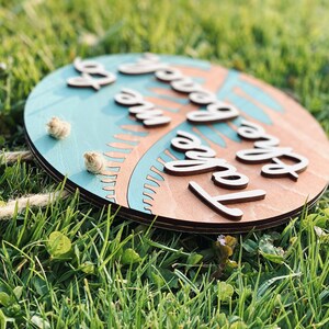 May include: Round wooden sign with the text "Take me to the beach" in a cursive font. The sign has a light blue center with a palm tree design and a natural wood border. Two small rope accents are attached.