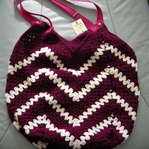 Könnte beinhalten: Eine gehäkelte Tragetasche mit einem Chevron-Muster in Burgunderrot und Weiß. Die Tasche hat einen rosafarbenen Trageriemen und ein kleines Etikett mit der Aufschrift "Handgefertigt mit Liebe".