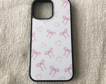 May include: A white phone case with a black border and a pattern of pink bows and hearts.