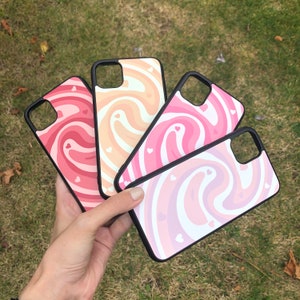 May include: Four phone cases with a swirl pattern in pink, peach, and white with small white hearts. The cases are black and have a raised edge.
