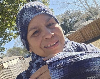 May include: A handmade crochet beanie and matching scarf set featuring a variegated yarn pattern in shades of navy blue, light blue, and grey. The textured knit accessories are crafted with a consistent stitch pattern throughout the set.