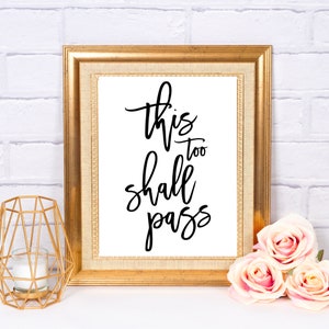 May include: A gold framed print with the text "This too shall pass" in black calligraphy on a white background.