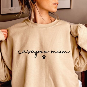 May include: A tan sweatshirt with the text "cavapoo mum" and a paw print in black.