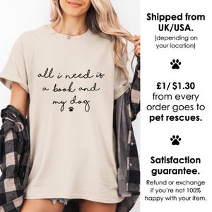 May include: A beige short-sleeved t-shirt featuring the black text "all i need is a book and my dog" with a small paw print icon. The shirt is worn with a black and white plaid flannel shirt layered over it, creating a casual layered look.