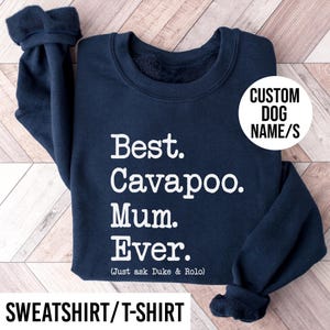 May include: Navy blue sweatshirt with white text: "Best. Cavapoo. Mum. Ever." and "(Just ask Duke & Rolo)". A white circle reads "CUSTOM DOG NAME/S". The bottom reads "SWEATSHIRT/T-SHIRT".
