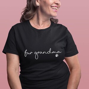 Puede incluir: Camiseta negra con la frase "fur grandma" en cursiva y una huella de pata. La camiseta es de un material suave y tiene un estilo casual.