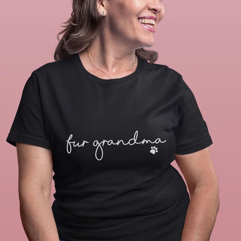 Puede incluir: Camiseta negra con la frase "fur grandma" en cursiva y una huella de pata. La camiseta es de un material suave y tiene un estilo casual.