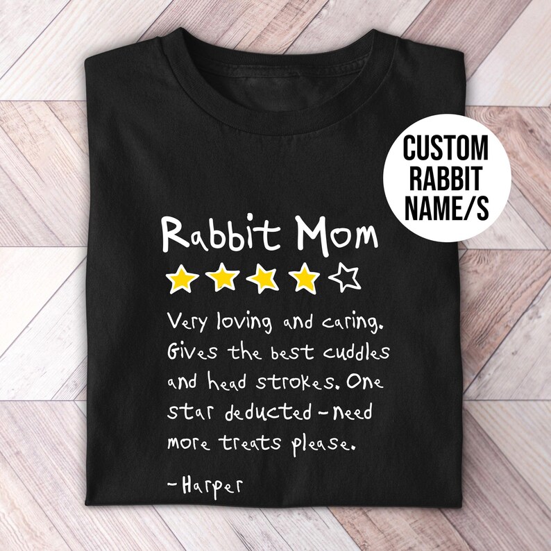 May include: A black t-shirt featuring the white text Rabbit Mom, four yellow stars, and one white star outline. Below, white text reads: Very loving and caring. Gives the best cuddles and head strokes. One star deducted - need more treats please. - Harper.