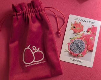 May include: A red velvet pouch with a white logo that says "foodhealingdeck.com" and two white stylized pears. The pouch is next to a white card with the words "Dragon Fruit" and "Surprise" printed on it. The card has a picture of a dragon fruit.