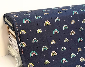 Tela de punto para niños con arcoíris y detalle de lámina dorada sobre una base azul marino suave y elástica. Se vende por medio metro.