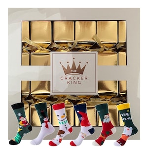 May include: A Christmas gift set featuring gold-wrapped crackers and six festive socks. The socks display seasonal designs like Santa, snowmen, and holiday motifs. The box is labelled "THE CRACKER KING", a festive gift idea.