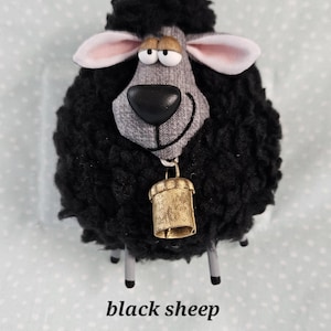May include: A plush black sheep figurine with a gray face, pink-lined ears, and a gold bell. The sheep has a fluffy wool-like texture and four silver legs. The text "black sheep" is printed below the figurine.