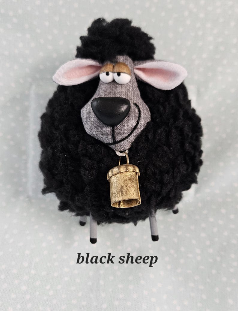 May include: A plush black sheep figurine with a gray face, pink-lined ears, and a gold bell. The sheep has a fluffy wool-like texture and four silver legs. The text "black sheep" is printed below the figurine.