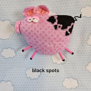 May include: A pink stuffed pig with black spots, pink legs, and a curly tail. The pig has large, expressive eyes and ears. The text "black spots" is below the pig.