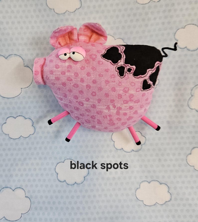 May include: A pink stuffed pig with black spots, pink legs, and a curly tail. The pig has large, expressive eyes and ears. The text "black spots" is below the pig.