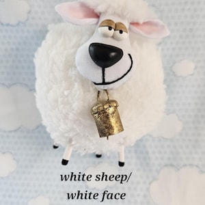 May include: A plush white sheep figurine with a smiling face, black eyes, and a gold bell around its neck. The sheep has a fluffy body and pink-lined ears. The text "white sheep/white face" is at the bottom.