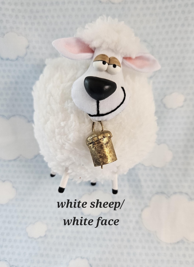May include: A plush white sheep figurine with a smiling face, black eyes, and a gold bell around its neck. The sheep has a fluffy body and pink-lined ears. The text "white sheep/white face" is at the bottom.