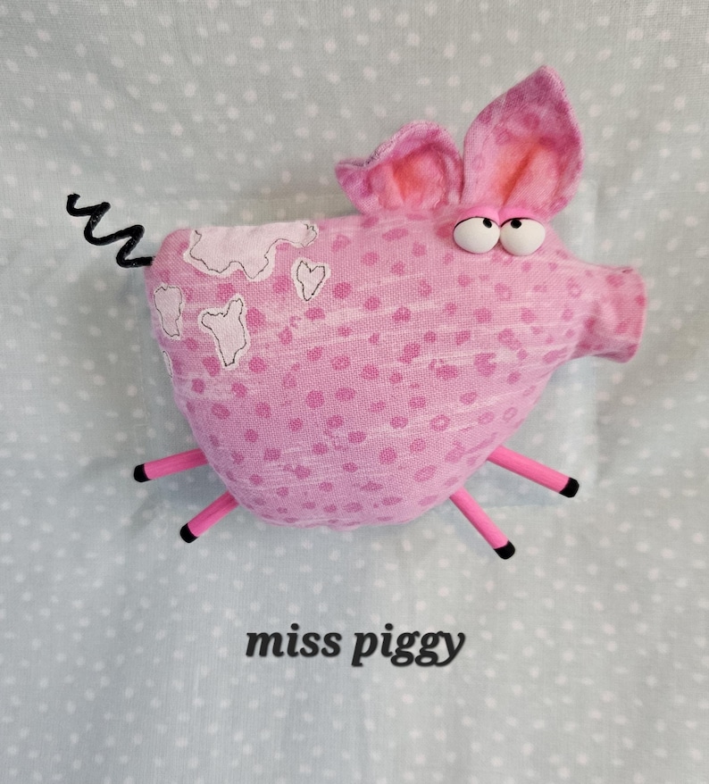 May include: A pink stuffed pig with large ears, googly eyes, and a curly tail. The pig has pink polka dots and white patches. The text "miss piggy" is printed below the pig.