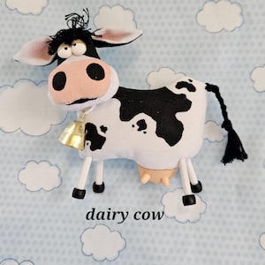 May include: A stuffed dairy cow with a bell around its neck. The cow is white with black spots and a pink nose. The text "dairy cow" is below the cow.
