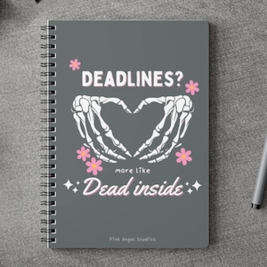 May include: Gray spiral bound notebook with a black skeleton hand design forming a heart shape. The text reads "Deadlines? More like Dead inside." with pink flowers and glitter accents. The bottom of the notebook says "Pink Angel Studios."