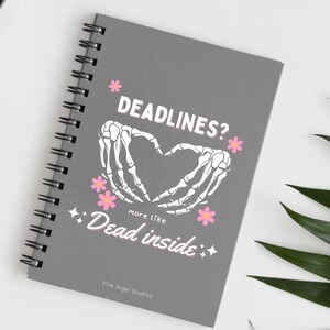 May include: Gray spiral bound notebook with a white skeleton hand design forming a heart shape. The text "Deadlines? more like Dead inside" is printed in pink on the front cover.
