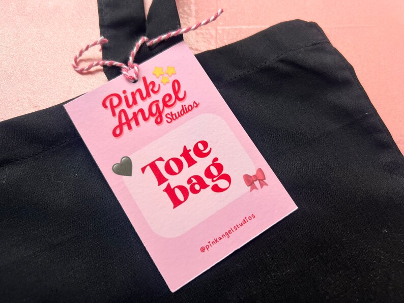 Puede incluir: Bolsa de tela Pink Angel Studios con fondo rosa y texto rojo. El texto dice "Tote Bag" y el nombre de la empresa en las redes sociales es "@pinkangelstudios".