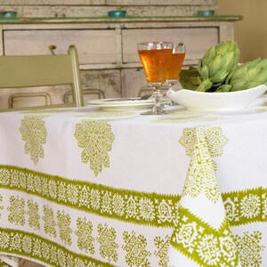 May include: White tablecloth with a green geometric pattern. The tablecloth has a border of green and white geometric designs. Two glasses of orange liquid and a bowl of artichokes are on the table.